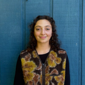 The Sylvia Center Chef Educator Jess Shulman poses smiling against a blue wall